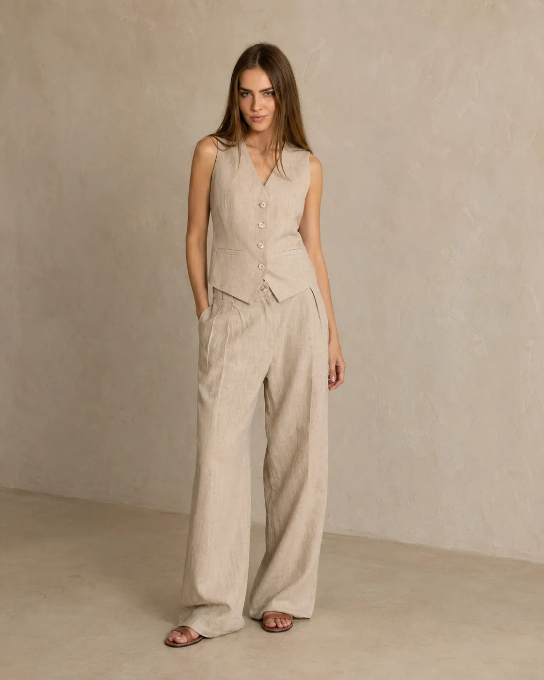 Een model draagt de kaki mouwloze top en wijde broek, met één hand in haar zak.