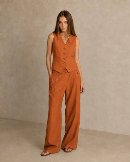 Een model draagt de oranje mouwloze top en broek met lage taille, staand in een ontspannen vooraanzicht.
