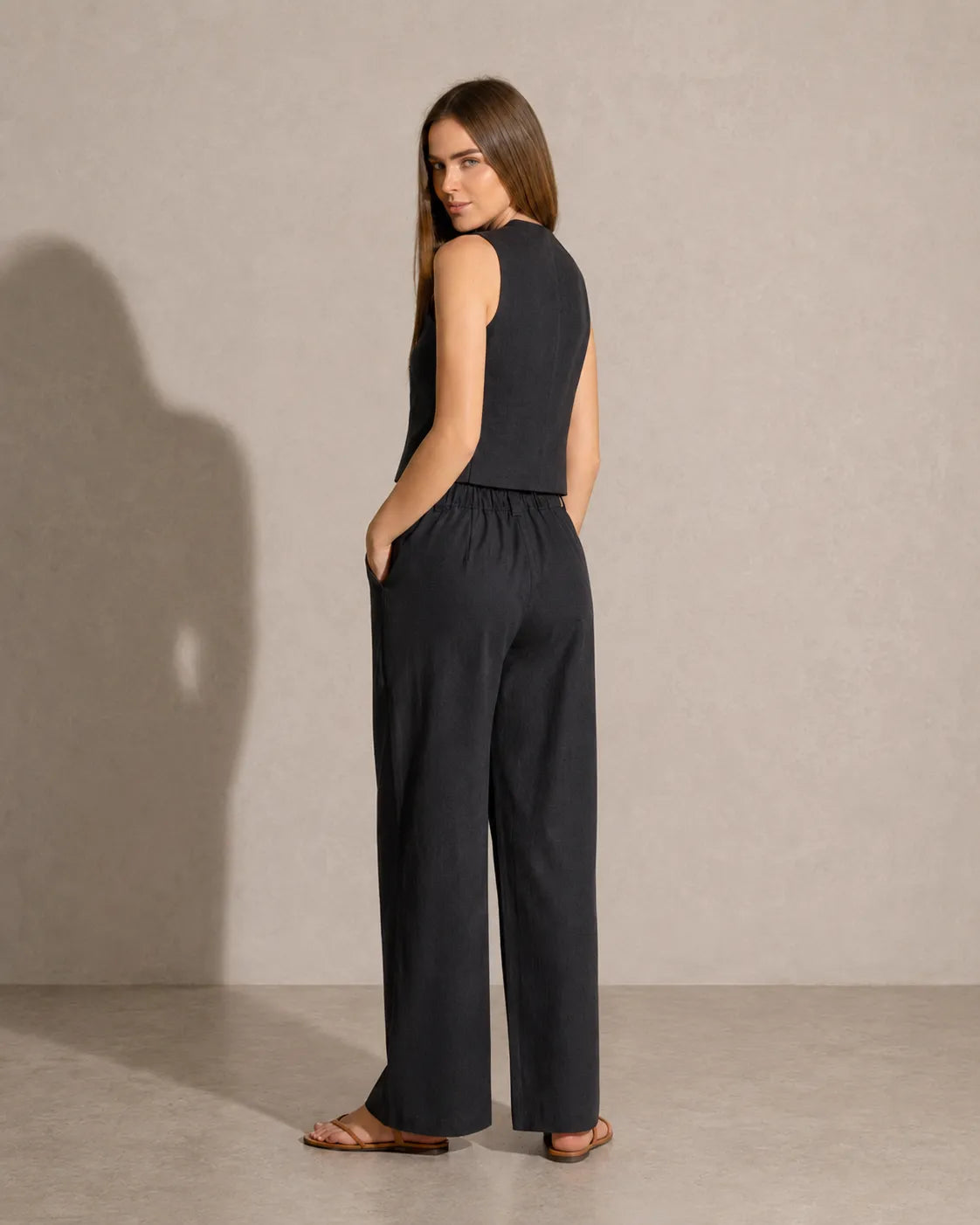 Achteraanzicht van een model in de zwarte co-ord set, met zicht op de taillelband van de broek met lage taille.