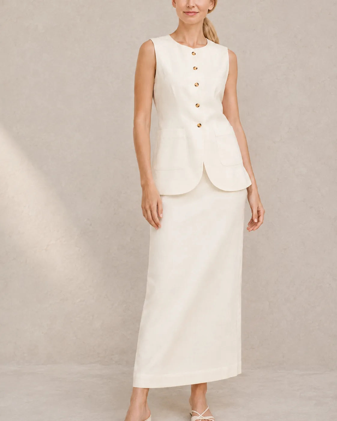 Een model draagt de gebroken witte mouwloze top en hoge taille maxirok, staand in een ontspannen vooraanzicht.