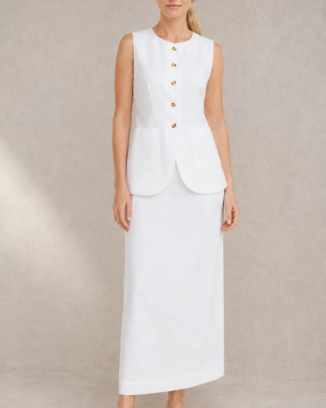 Een close-up vooraanzicht van een model in de witte mouwloze top en hoge taille maxirok.