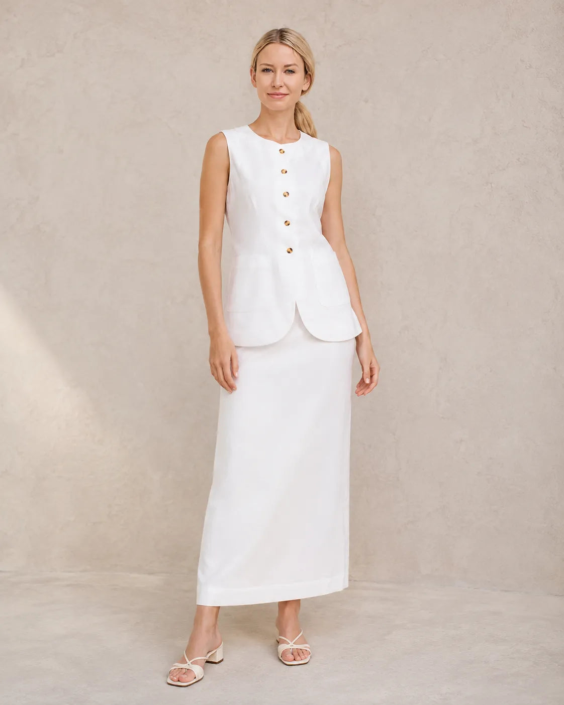 Een model draagt de witte mouwloze top en hoge taille maxirok, staand in een ontspannen vooraanzicht.