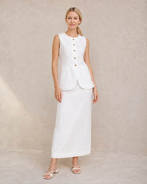 Een model draagt de witte mouwloze top en hoge taille maxirok, staand in een ontspannen vooraanzicht.