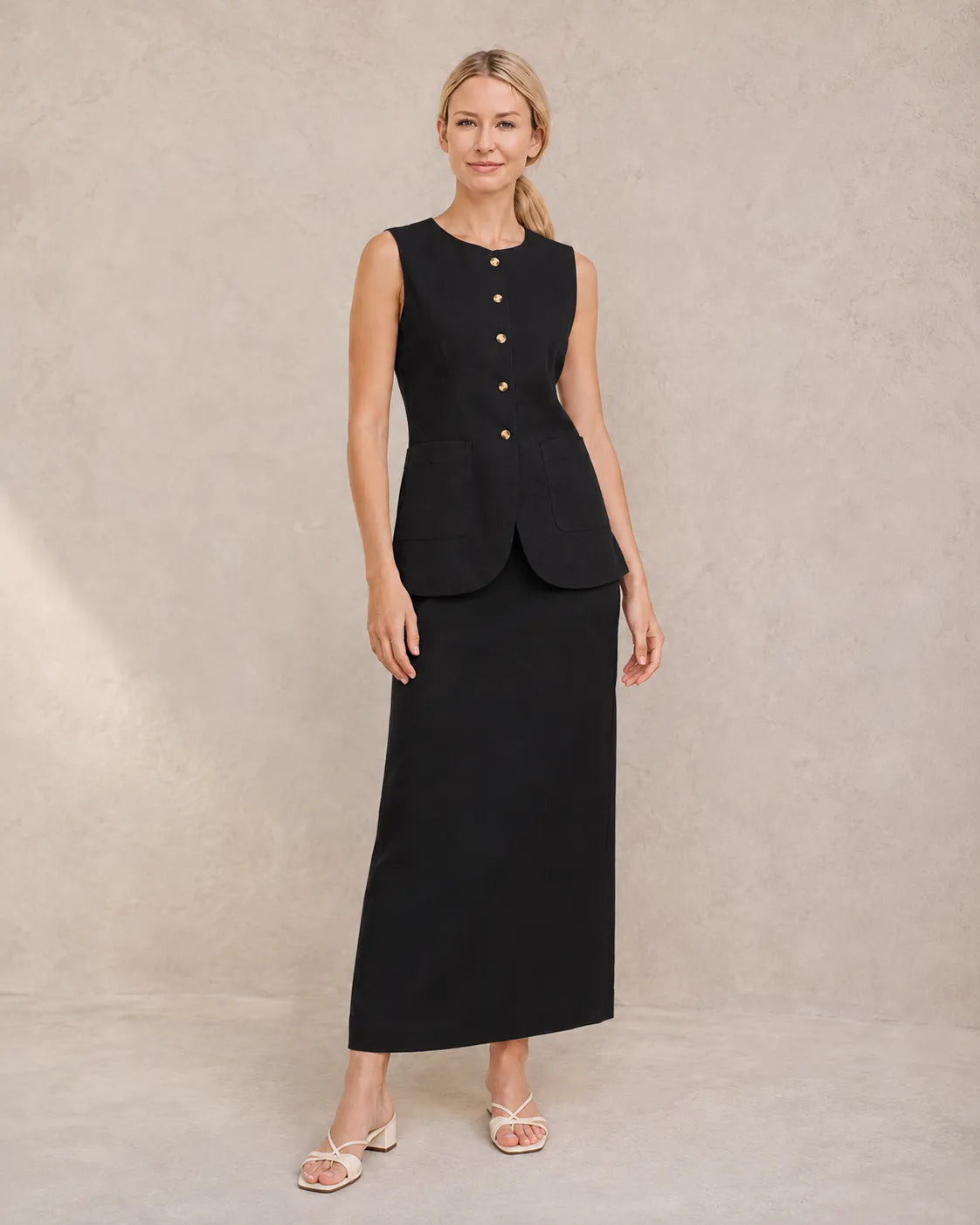 Een model draagt de zwarte mouwloze top en hoge taille maxirok, staand in een ontspannen vooraanzicht.